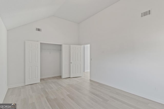 unfurnished bedroom featuring light hardwood / wood-style floors, high vaulted ceiling, and a closet