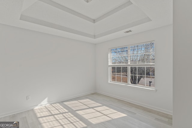 unfurnished room with light wood-type flooring and a raised ceiling