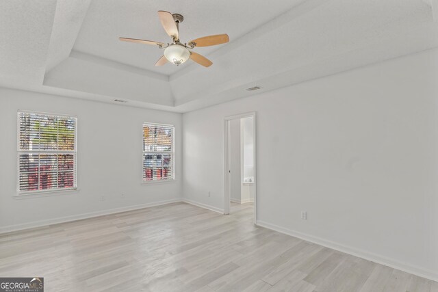 unfurnished room featuring a raised ceiling, ceiling fan, and light hardwood / wood-style floors