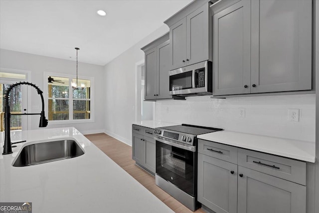 kitchen with sink, gray cabinetry, decorative light fixtures, stainless steel appliances, and backsplash