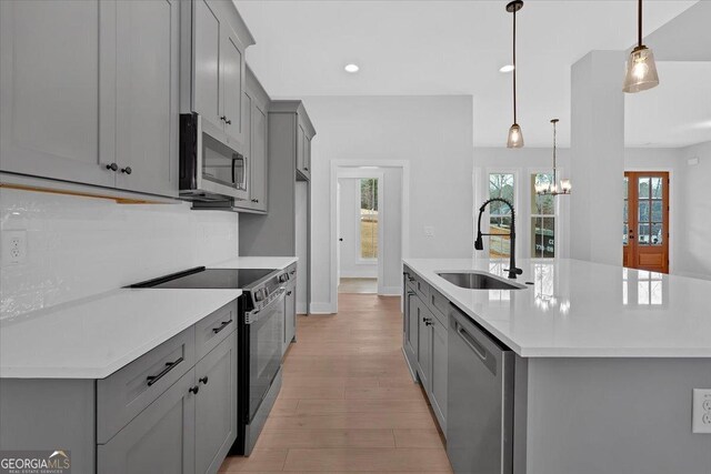 kitchen with sink, a center island with sink, gray cabinets, pendant lighting, and stainless steel appliances