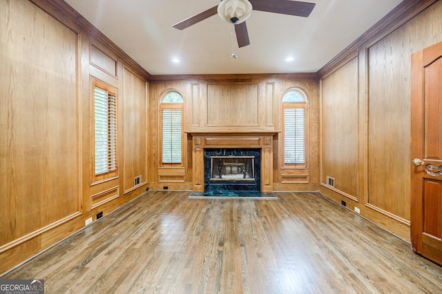 unfurnished living room featuring a high end fireplace, a healthy amount of sunlight, ceiling fan, and wooden walls