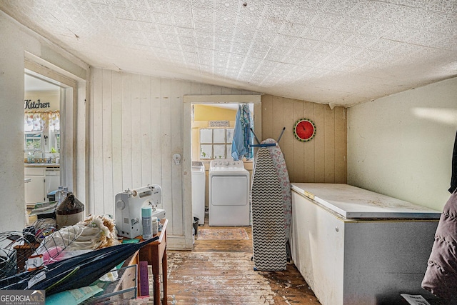 laundry area featuring hardwood / wood-style flooring, washing machine and dryer, sink, and wooden walls