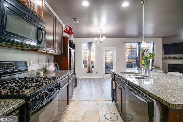 kitchen featuring pendant lighting, a kitchen island with sink, black appliances, sink, and a notable chandelier