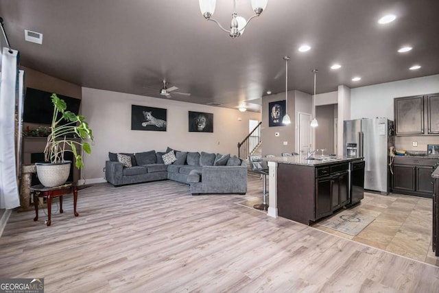 kitchen with a kitchen island with sink, stainless steel refrigerator with ice dispenser, decorative light fixtures, light stone counters, and dark brown cabinetry