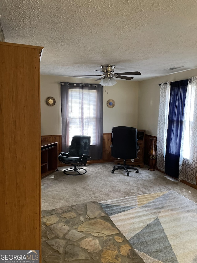 office area with a textured ceiling, carpet floors, ceiling fan, and wood walls