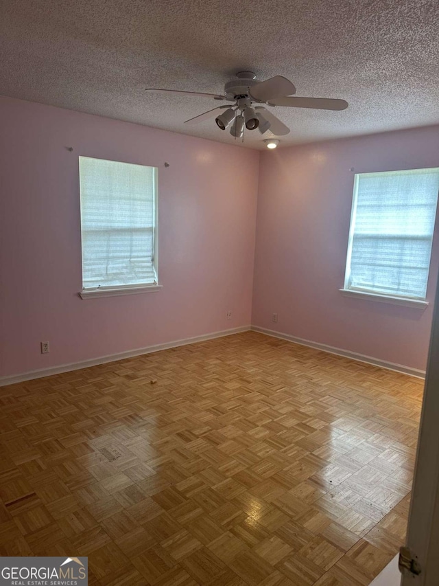 spare room featuring a textured ceiling, light parquet floors, a wealth of natural light, and ceiling fan