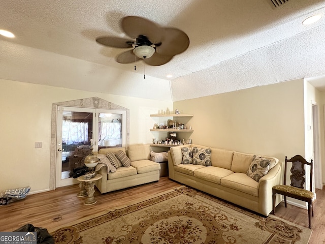 living room with ceiling fan, light hardwood / wood-style flooring, a textured ceiling, and vaulted ceiling