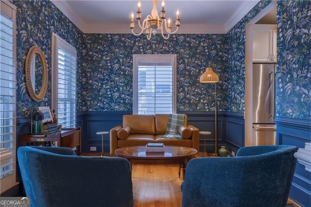 living area with a wealth of natural light, hardwood / wood-style floors, ornamental molding, and a notable chandelier