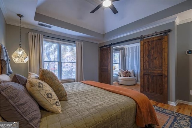 bedroom with a raised ceiling, ceiling fan, crown molding, wood-type flooring, and a barn door