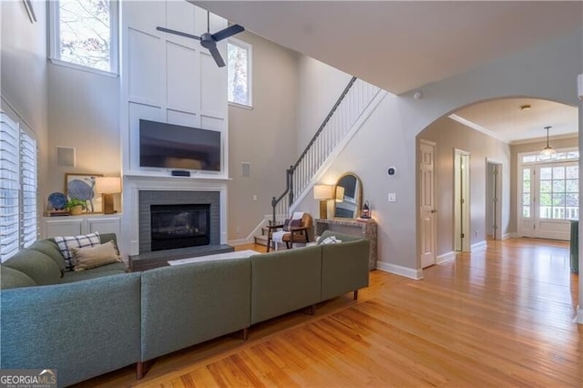 living room featuring a fireplace, light wood-type flooring, ceiling fan, and crown molding