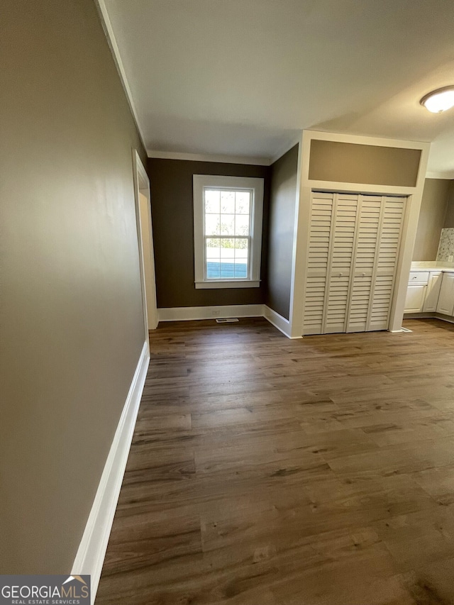 unfurnished bedroom with dark hardwood / wood-style floors, crown molding, and a closet