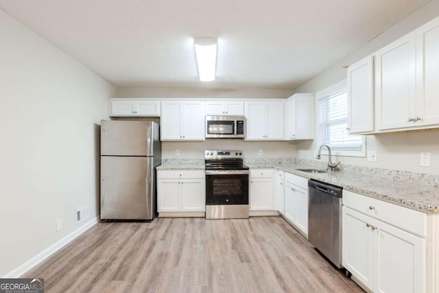 kitchen featuring light stone countertops, white cabinetry, sink, stainless steel appliances, and light wood-type flooring