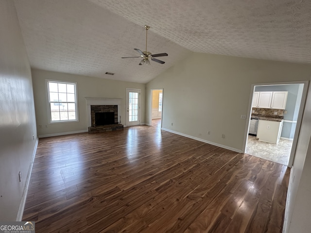 unfurnished living room featuring a textured ceiling, ceiling fan, dark wood-type flooring, a stone fireplace, and lofted ceiling