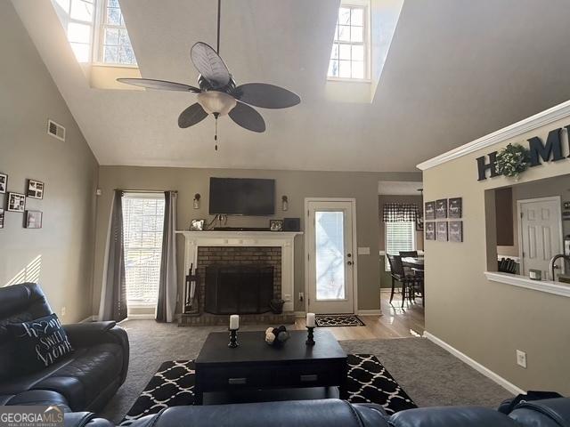 living room with ceiling fan, a fireplace, high vaulted ceiling, and light carpet