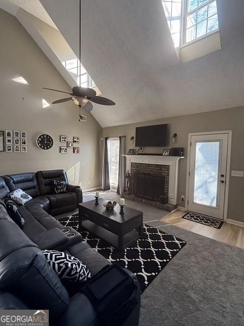 living room featuring ceiling fan, light hardwood / wood-style flooring, high vaulted ceiling, and a brick fireplace