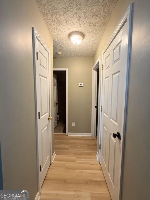 hallway with a textured ceiling and light hardwood / wood-style flooring