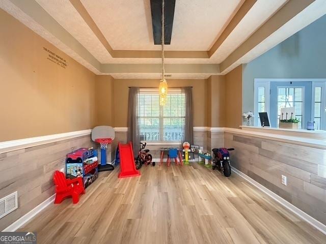 rec room featuring hardwood / wood-style floors, a raised ceiling, and wooden walls