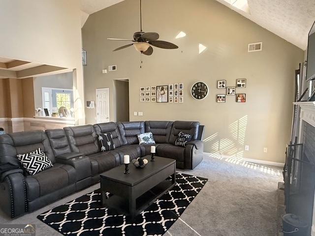 carpeted living room with ceiling fan and high vaulted ceiling