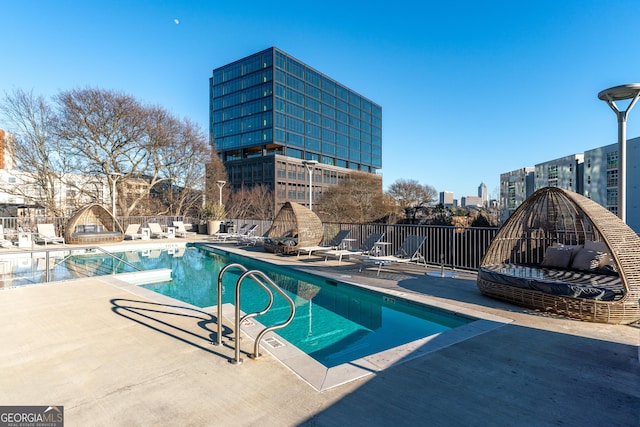 community pool featuring a view of city, a patio, and fence