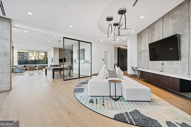 living room with a chandelier, recessed lighting, an accent wall, light wood-type flooring, and floor to ceiling windows