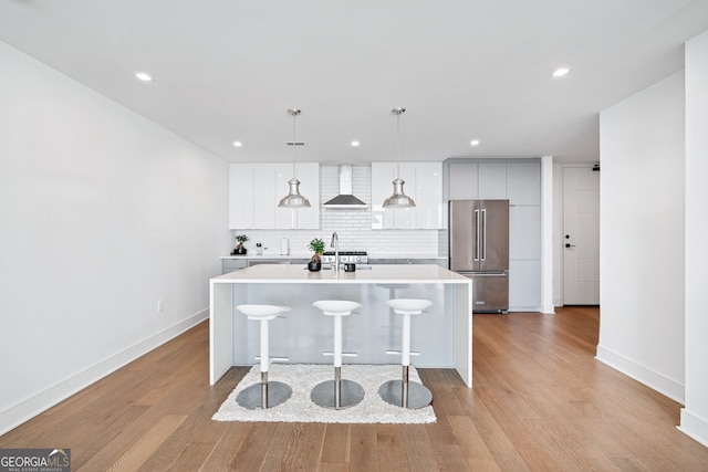 kitchen with high quality fridge, a kitchen breakfast bar, light countertops, wall chimney exhaust hood, and decorative light fixtures