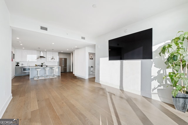 unfurnished living room with baseboards, light wood-type flooring, visible vents, and recessed lighting