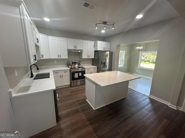 kitchen with light stone counters, stainless steel appliances, sink, white cabinetry, and a kitchen island