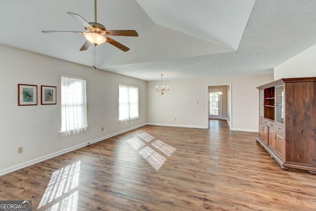 unfurnished living room featuring lofted ceiling, a healthy amount of sunlight, ceiling fan with notable chandelier, and light wood-type flooring