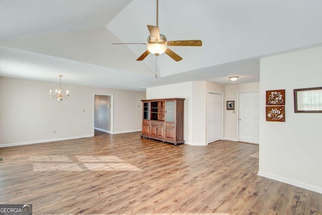 unfurnished living room with ceiling fan with notable chandelier, light hardwood / wood-style floors, and vaulted ceiling