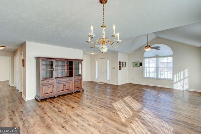 unfurnished living room featuring ceiling fan with notable chandelier, light hardwood / wood-style floors, and vaulted ceiling