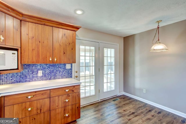 kitchen featuring hardwood / wood-style floors, decorative backsplash, hanging light fixtures, and a textured ceiling