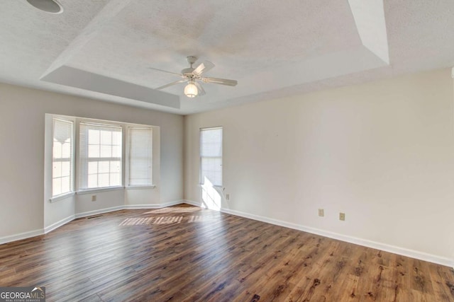 empty room with a raised ceiling, ceiling fan, dark hardwood / wood-style flooring, and a textured ceiling