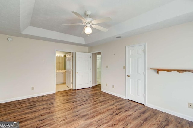 unfurnished bedroom featuring a tray ceiling, ceiling fan, hardwood / wood-style flooring, and ensuite bathroom