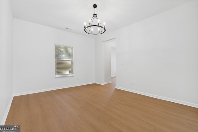 spare room featuring a notable chandelier and light wood-type flooring