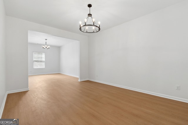 spare room with an inviting chandelier and wood-type flooring