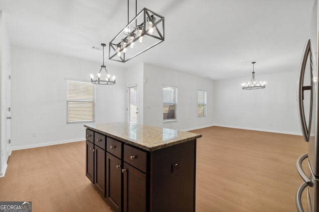 kitchen featuring dark brown cabinets, hanging light fixtures, light hardwood / wood-style flooring, a kitchen island, and light stone countertops