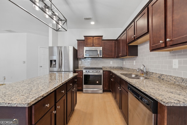 kitchen featuring sink, tasteful backsplash, a kitchen island, stainless steel appliances, and light stone countertops