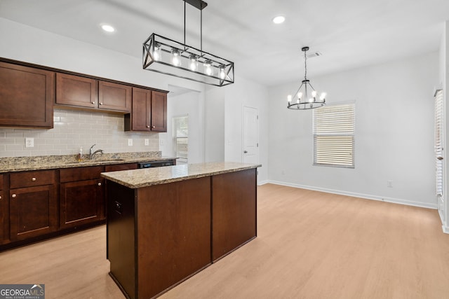 kitchen with pendant lighting, light hardwood / wood-style flooring, a center island, light stone counters, and decorative backsplash