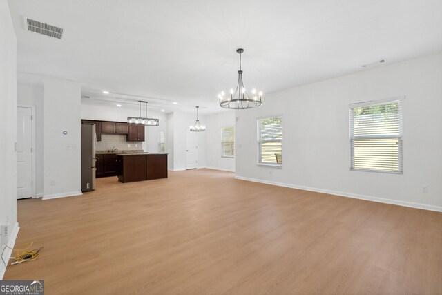 unfurnished living room featuring a notable chandelier and light hardwood / wood-style floors