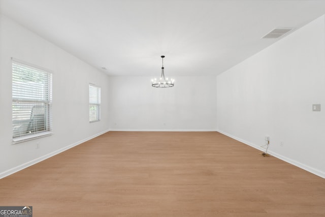 spare room featuring a notable chandelier and light wood-type flooring