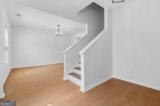 staircase with wood-type flooring and a notable chandelier