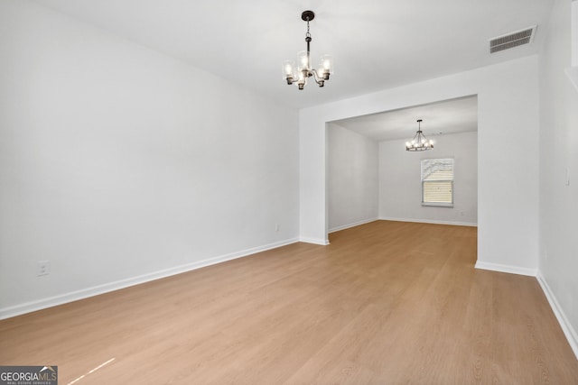 spare room with light wood-type flooring and a notable chandelier