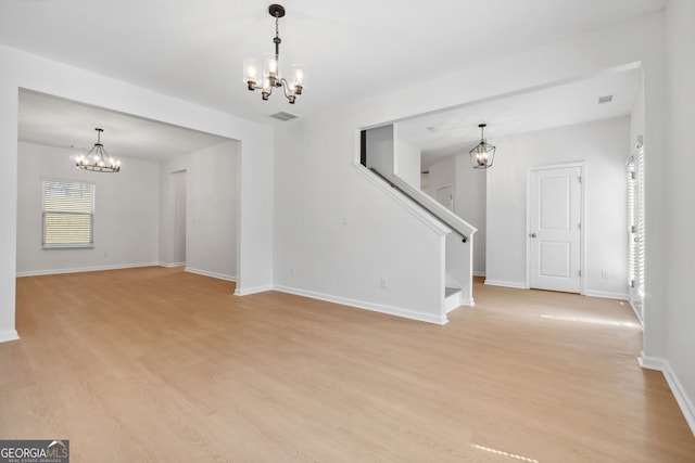 empty room with light wood-type flooring and a notable chandelier