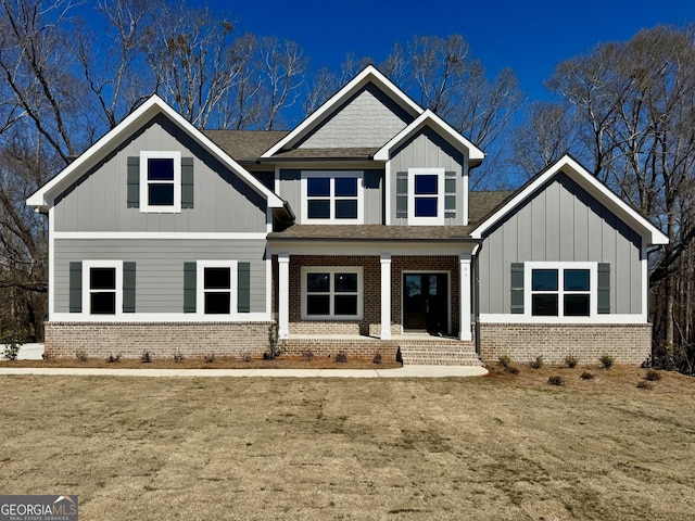 craftsman-style home featuring roof with shingles, brick siding, board and batten siding, and a front yard