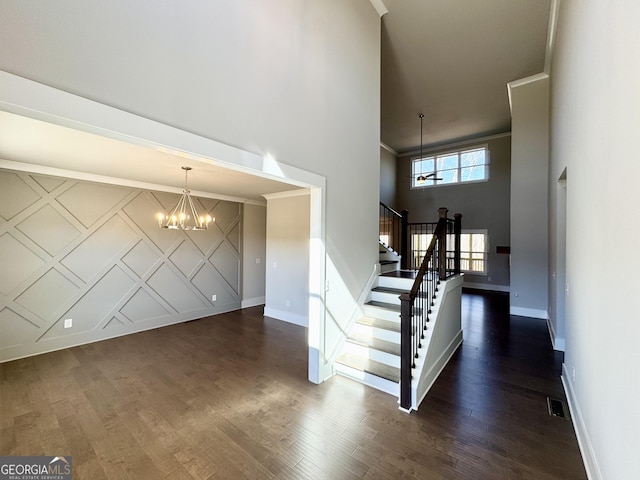 entrance foyer with an accent wall, dark wood-style flooring, ornamental molding, stairway, and an inviting chandelier