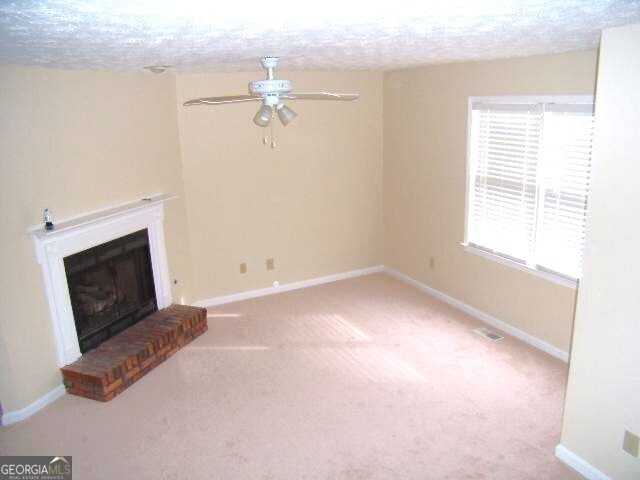 unfurnished living room with carpet flooring, ceiling fan, plenty of natural light, and a brick fireplace