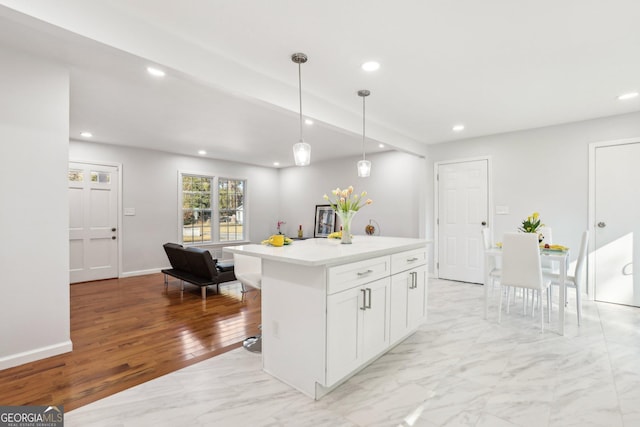 kitchen with white cabinetry, a kitchen breakfast bar, light hardwood / wood-style floors, decorative light fixtures, and a kitchen island