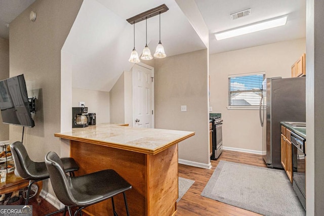 kitchen featuring hanging light fixtures, light hardwood / wood-style flooring, appliances with stainless steel finishes, a kitchen bar, and kitchen peninsula