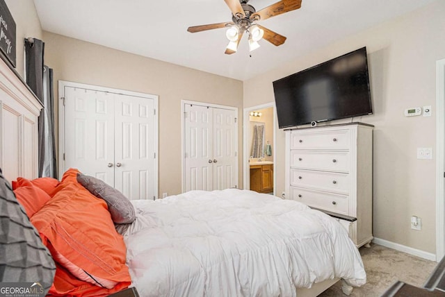 carpeted bedroom featuring ensuite bath, ceiling fan, and two closets